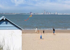 Une plage avec, en arrière-plan, la silhouette d’une ville, un bâtiment avec un toit bleu et des personnes sur le sable.