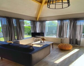 A modern living room with a black sofa, a TV, a coffee table, and a large window with curtains. - House in Breskens Near Scenic Beaches (Breskens)