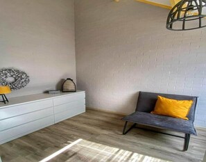 A modern living room with a white dresser, a grey sofa with a yellow cushion, a decorative wreath, and a hanging light fixture. - House in Breskens Near Scenic Beaches (Breskens)