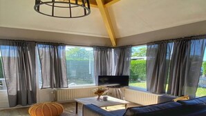 Een moderne woonkamer met een bank, een televisie, een tafel en een groot raam met gordijnen.