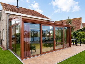 Una casa con un patio cubierto de cristal, fachada de ladrillo y techo de tejas.