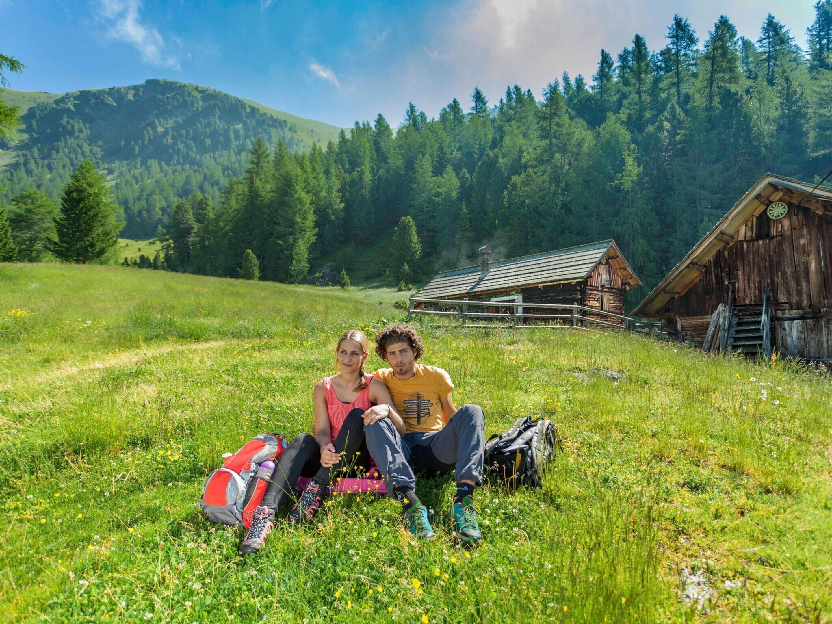 A couple sitting on a grassy field with a wooden cabin in the background.