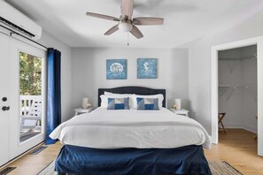 Une chambre à coucher avec un lit, un ventilateur de plafond, deux œuvres d’art murales et une vue sur l’extérieur.