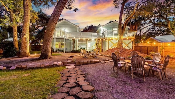A two-story house with a patio area, outdoor seating, and a staircase leading to a deck.