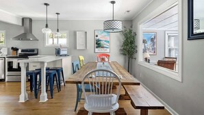 A modern kitchen with a dining area, featuring a wooden table, blue bar stools, and pendant lighting.