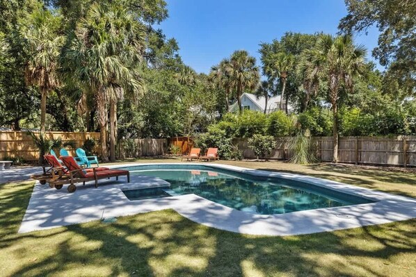 Un jardin à l’arrière de la maison, avec une piscine, entouré de palmiers et délimité par une clôture en bois.