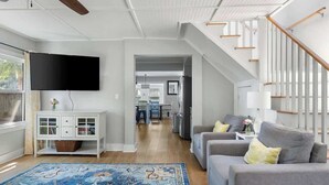 A modern living room with a flat-screen TV, grey sofas, a patterned rug, and a staircase.