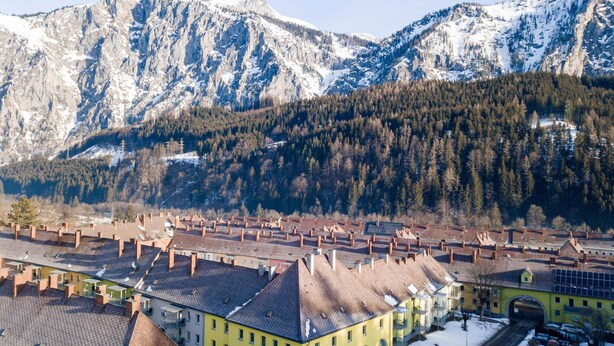 A town with traditional architecture, including buildings with sloped roofs and chimneys, set against a backdrop of snow-covered mountains and dense forests. - Styria Apartment With Mountain Views (Eisenerz)