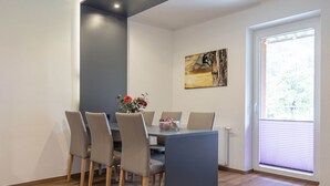A dining area with a table and chairs, a painting on the wall, and a window with blinds. - Styria Apartment With Mountain Views (Eisenerz)