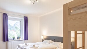 A bedroom with a wooden bed, a window with purple curtains, a bedside lamp, and a view of mountains. - Styria Apartment With Mountain Views (Eisenerz)