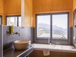 A modern bathroom with a large bathtub, a round sink, and a window offering a mountain view. - Cozy Chalet in Schladming With a Parking lot (Schladming)