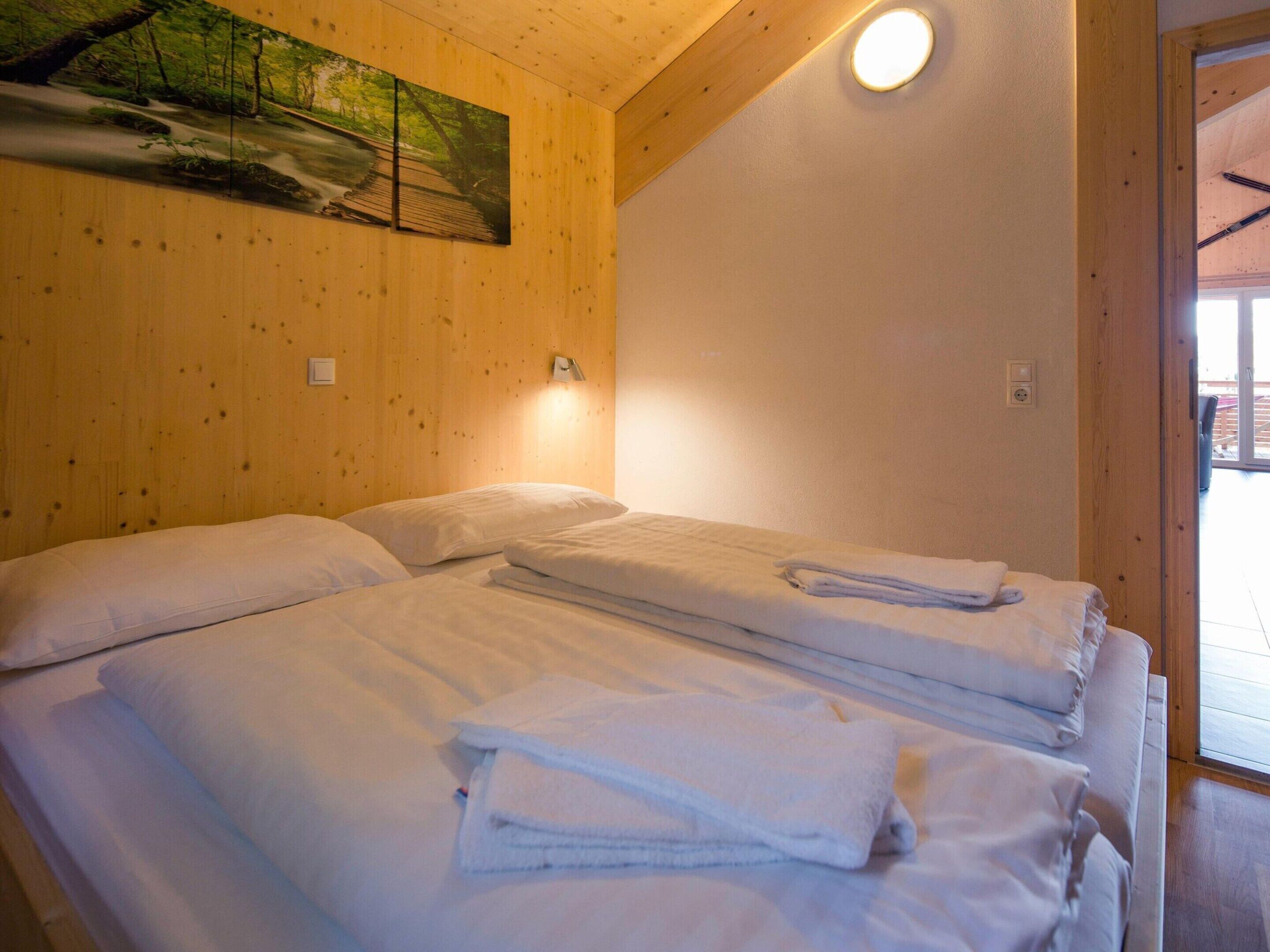 Una habitación con dos camas, paredes de madera, un cuadro de un bosque y una lámpara en el techo.