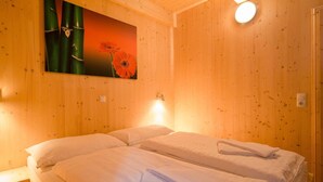 Una habitació amb parets de fusta, un llit amb roba blanca i un quadre de flors.