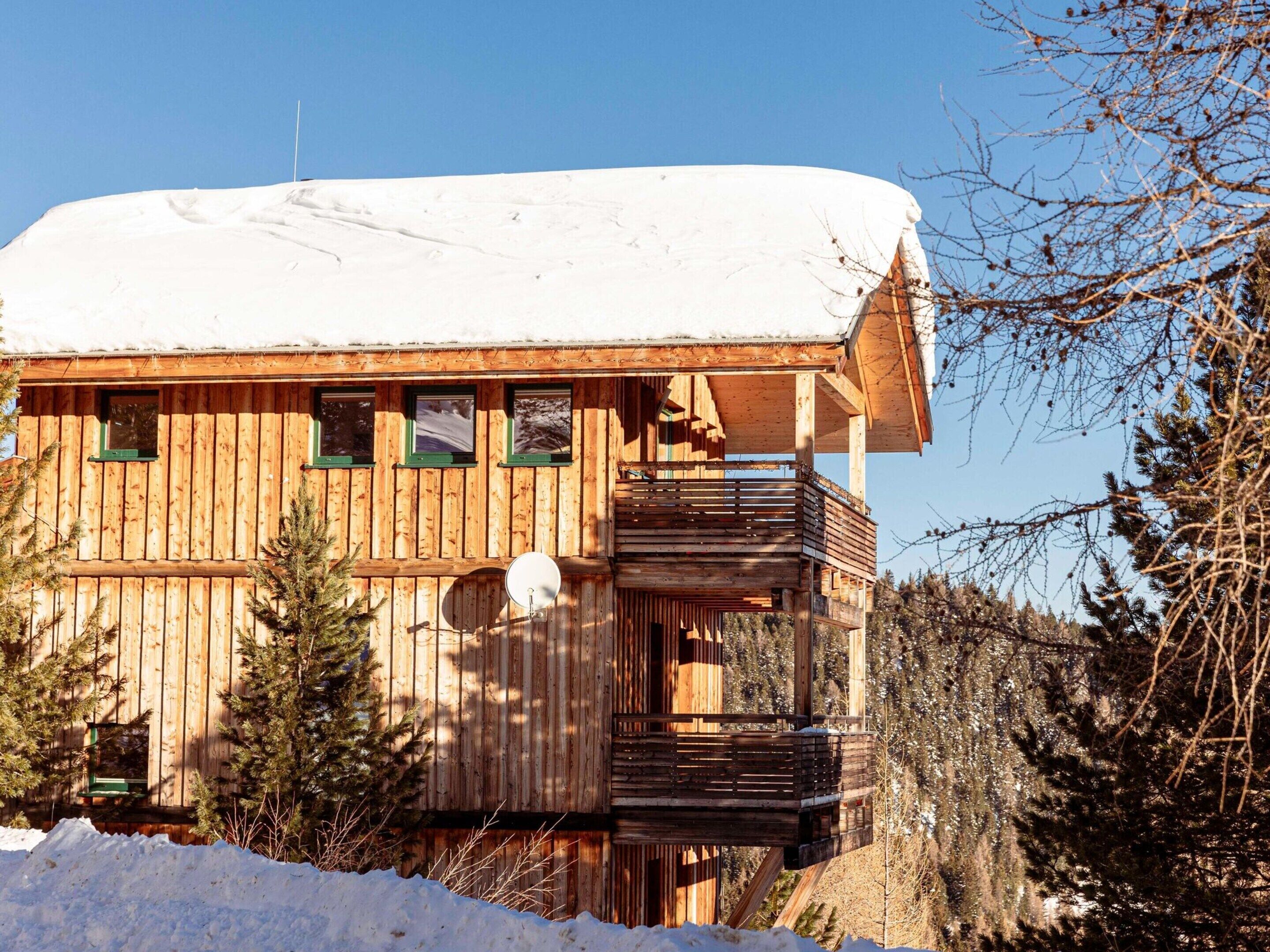 Una cabaña de madera con balcón, rodeada de nieve y árboles.