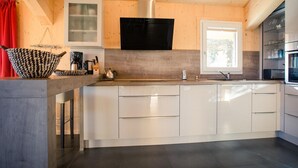 A modern kitchen with a central island, white cabinetry, a black range hood, and a window providing natural light. - Chalet Near Ski Resort in Austria With Sauna (Stadl-Predlitz)