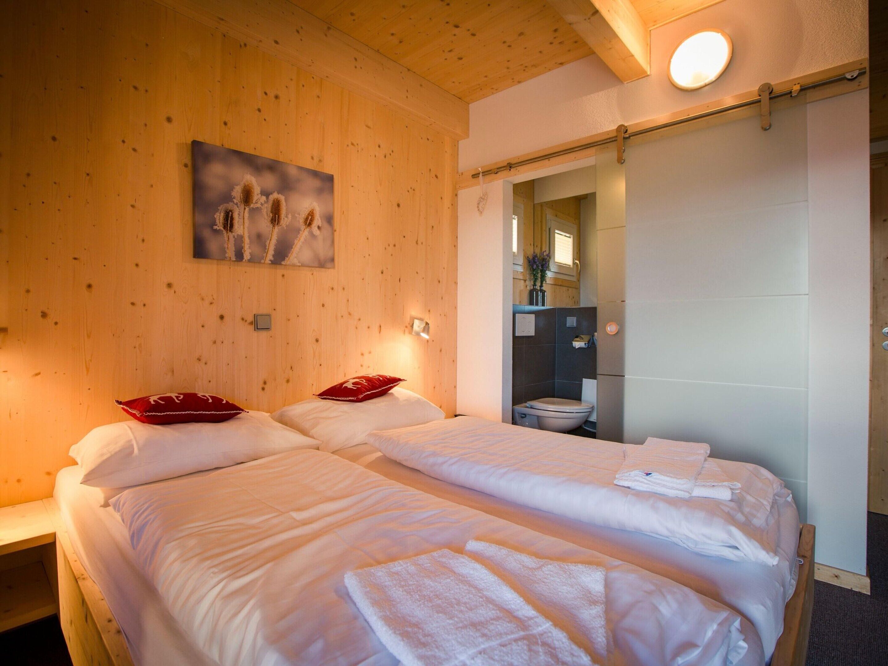 A hotel room with two beds, wooden walls, a painting, and a bathroom visible through an open door.