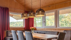 A wooden interior with a large table and chairs, red curtains, and a view of trees through the windows. - Chalet Near Ski Resort in Austria With Sauna (Stadl-Predlitz)