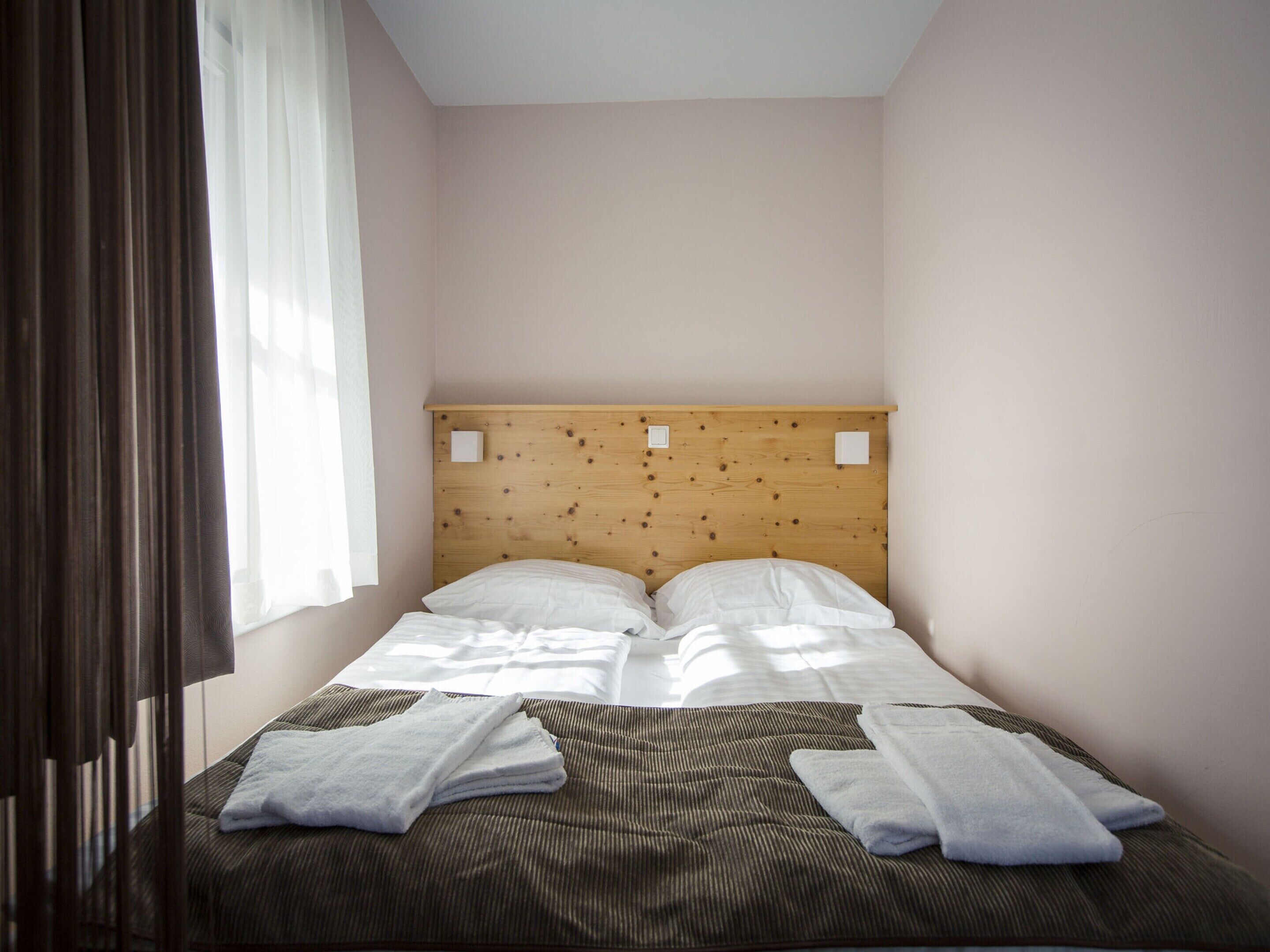 Un letto singolo con un poggiatesta in legno, due cuscini e un asciugamano piegato sopra il letto.