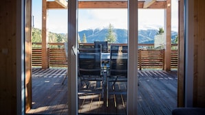 Un terrazzo in legno con una porta vetrata che dà su un balcone con vista su un paesaggio montano.