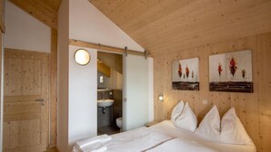 A bedroom with a wooden ceiling, a bed with white linens, a wooden door, and a bathroom visible through an open door. - Attractive Chalet With hot tub (Stadl-Predlitz)