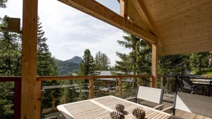 Eine Holzterrasse mit Tisch und Stühlen, mit Blick auf ein bewaldetes Tal und Berge.