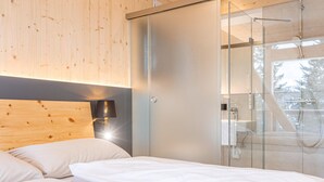 Une chambre moderne avec une tête de lit en bois, une cabine de douche en verre et une vue sur l’extérieur.