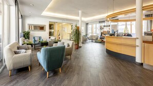 Un hall d’hôtel moderne avec un comptoir d’accueil, un espace salon et de grandes fenêtres.