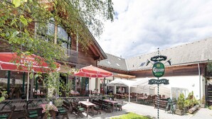 Un café en plein air avec des tables et des chaises en bois, des parasols rouges et une enseigne indiquant « Gösser ».