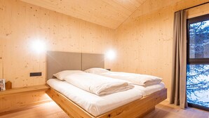 Una habitación tipo cabaña de madera con una cama, un ventanal con vistas a árboles y una lámpara en el techo.