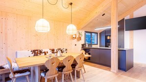 Un interior de madera con un comedor que incluye una mesa y sillas de madera, una cocina con electrodomésticos modernos, y vistas al exterior a través de una ventana.