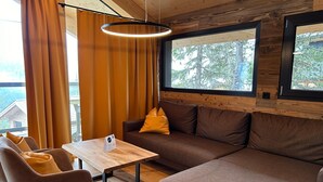 Una sala de estar moderna con piso de madera, un sofá marrón, una mesa de madera y una lámpara colgante.