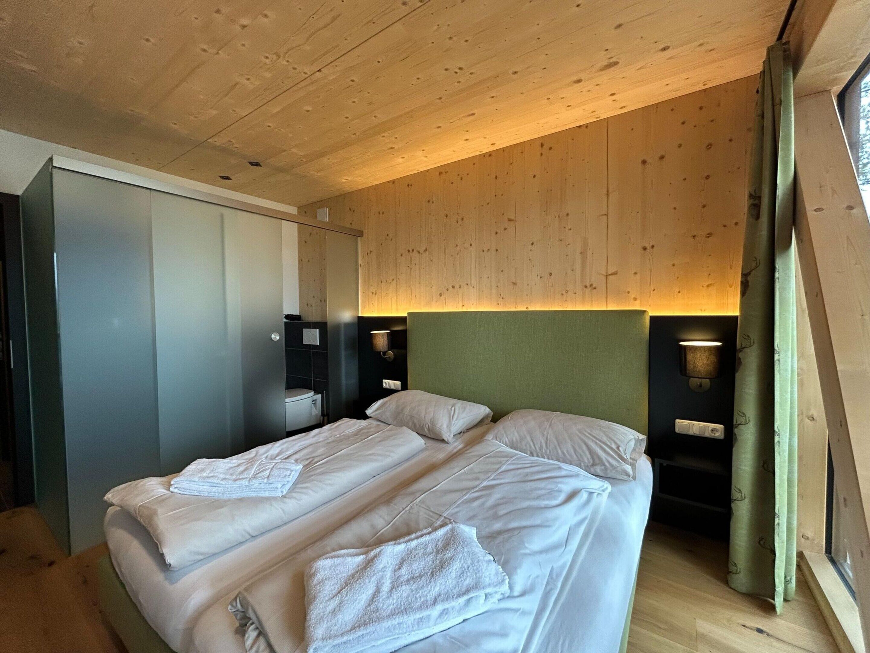 Un dormitorio con techo de madera, una cama con ropa de cama blanca, un cabecero verde y dos lámparas de noche.