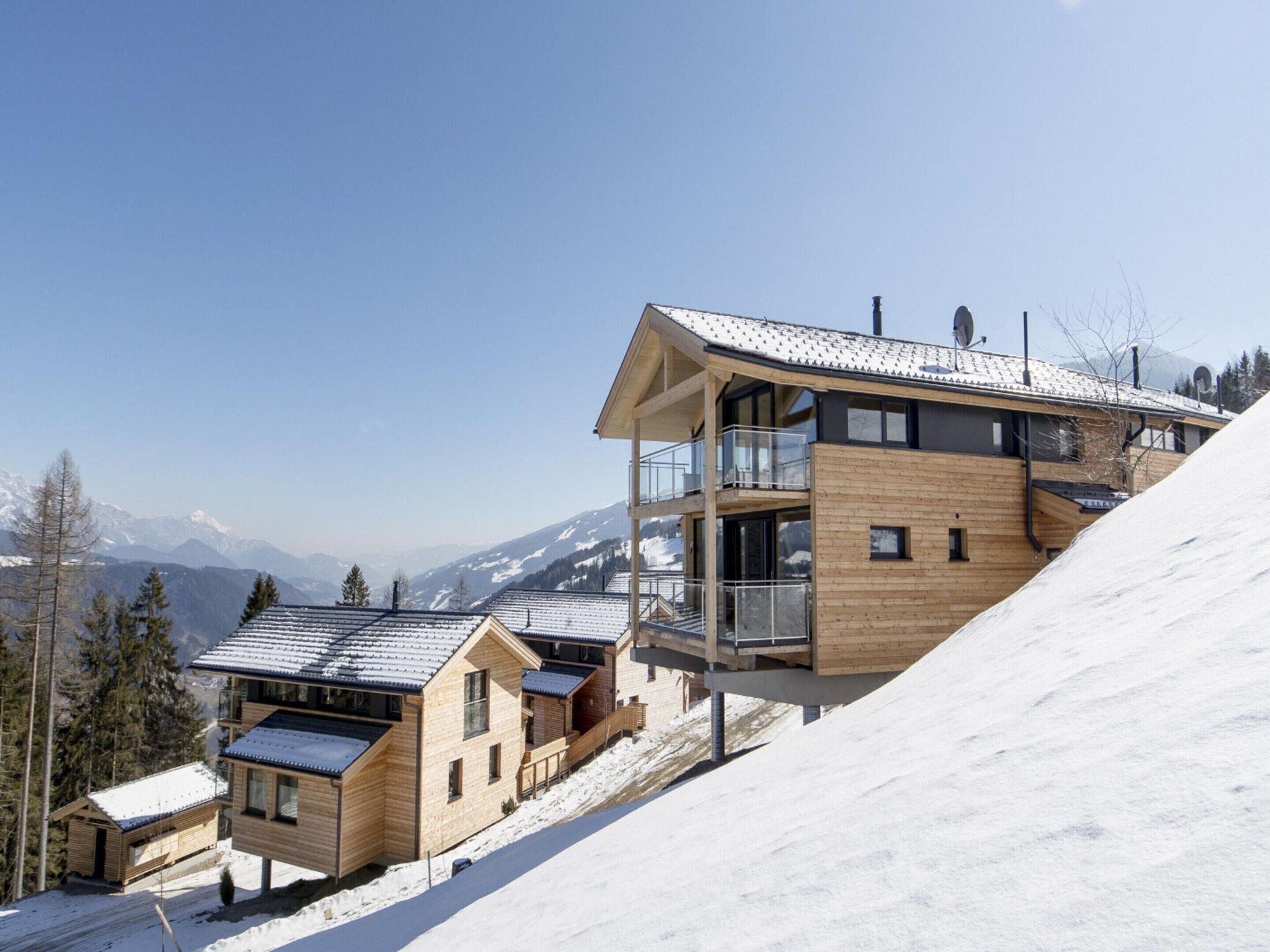 Un chalet moderne en bois, doté de nombreux balcons, qui se dresse sur fond de montagnes enneigées.