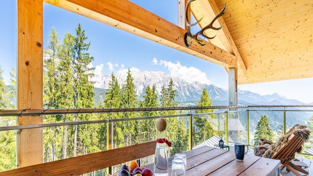 Une terrasse en bois avec une table, un saladier de fruits et une bouteille d’eau.