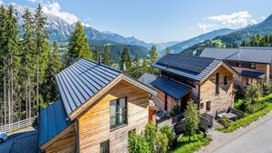 Une rangée de cabanes en bois aux toits inclinés, entourées d’une forêt et avec des montagnes en arrière-plan.