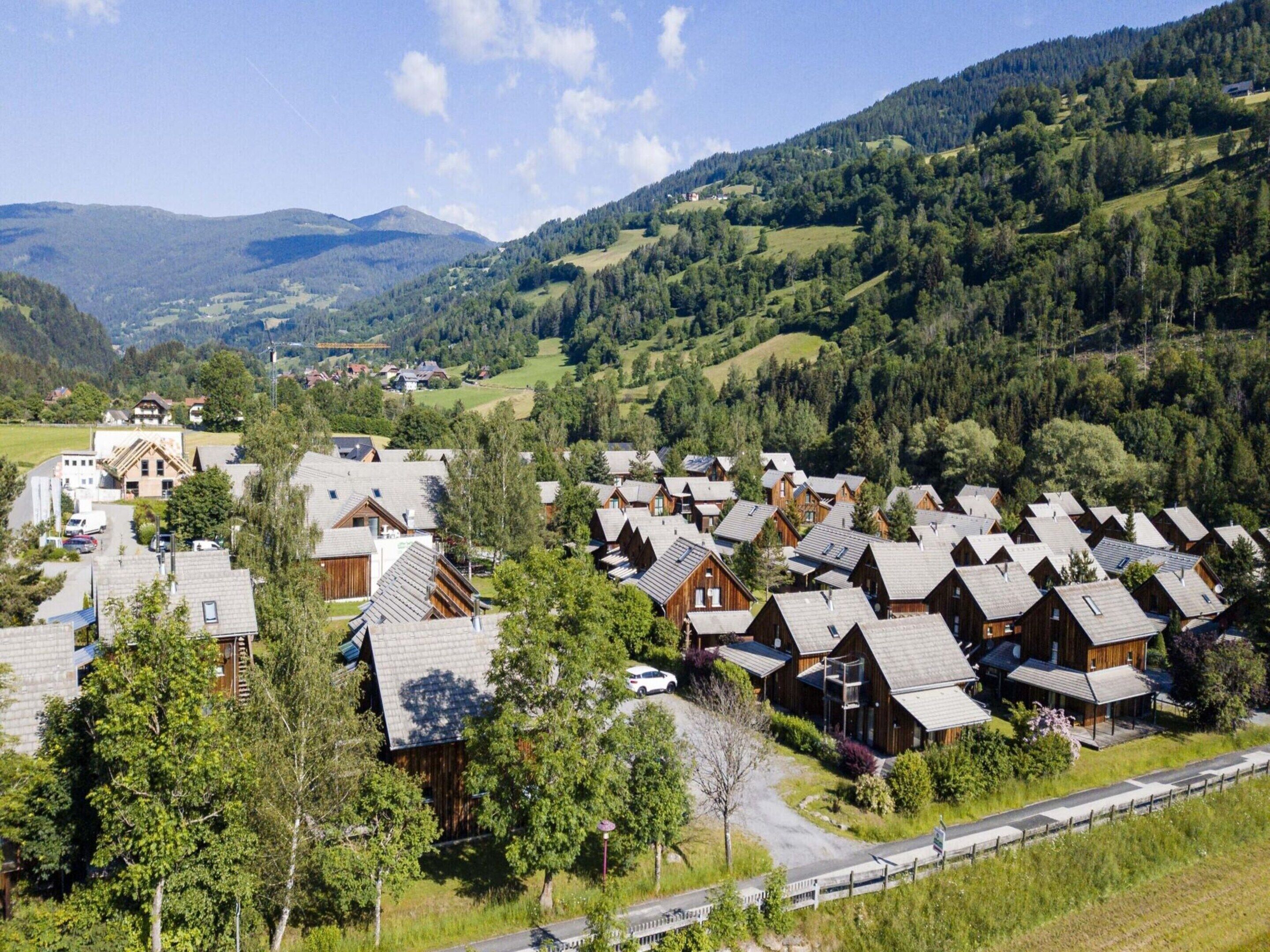 A cluster of wooden cabins with sloped roofs, surrounded by lush greenery and hills in the background.