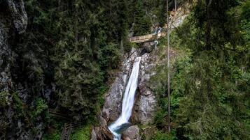 Una cascada en un área boscosa con un pasarela de madera que conduce a una plataforma de observación.
