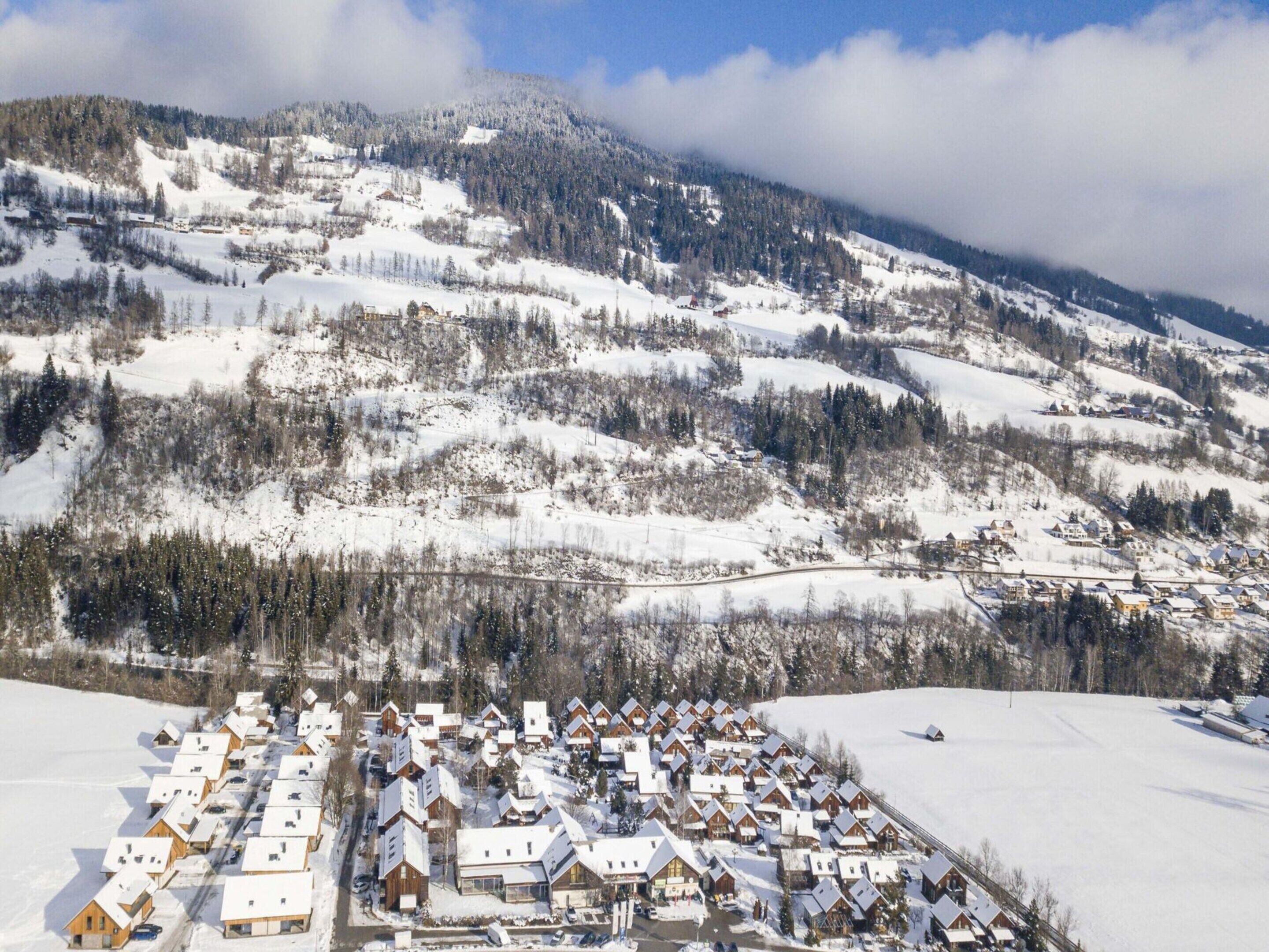 A snow-covered village with wooden houses, a winding road, and a mountain backdrop.