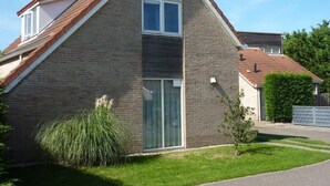 Ein zweistöckiges Haus mit Ziegelverkleidung, einem Satteldach und einem kleinen Vorgarten mit Rasen und ein paar Pflanzen.