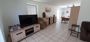 A living room with a TV, wooden entertainment unit, and a dining area with a table and chairs. - Eco Retreat by the Sea (Breskens)