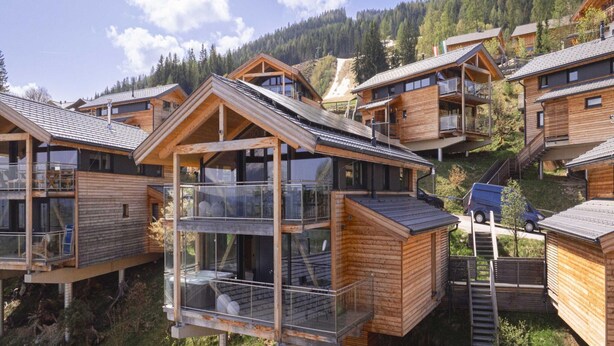 A modern wooden cabin with a glass balcony and a wooden deck, surrounded by a forested mountain area. - Appealing Chalet With Sauna (Schladming)