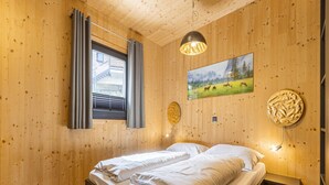 A wooden-paneled bedroom with a bed, a window with curtains, a painting of a landscape, and a wall-mounted light fixture. - Appealing Chalet With Sauna (Schladming)