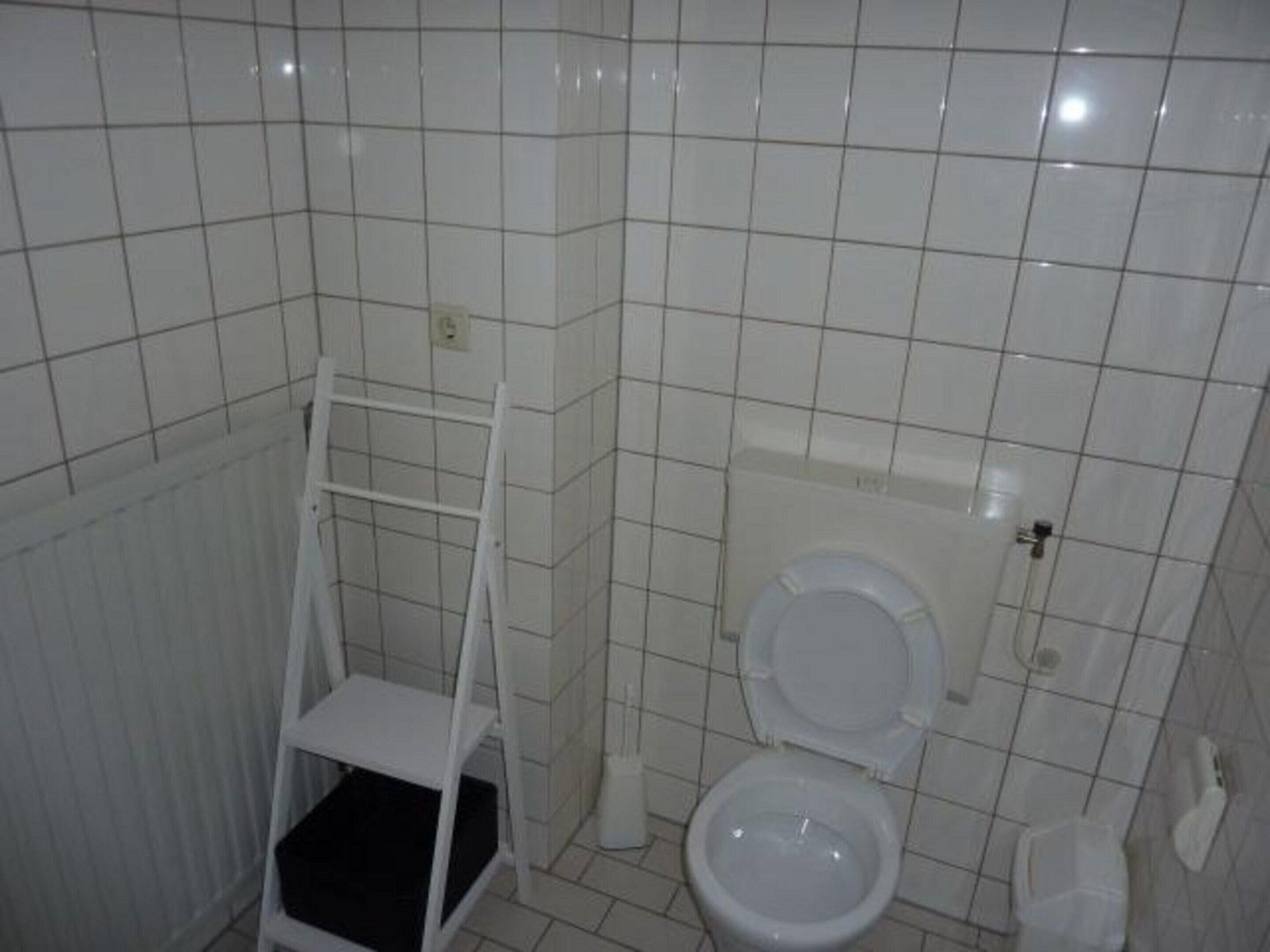 A small, tiled bathroom with a toilet, a white shelf, and a radiator.