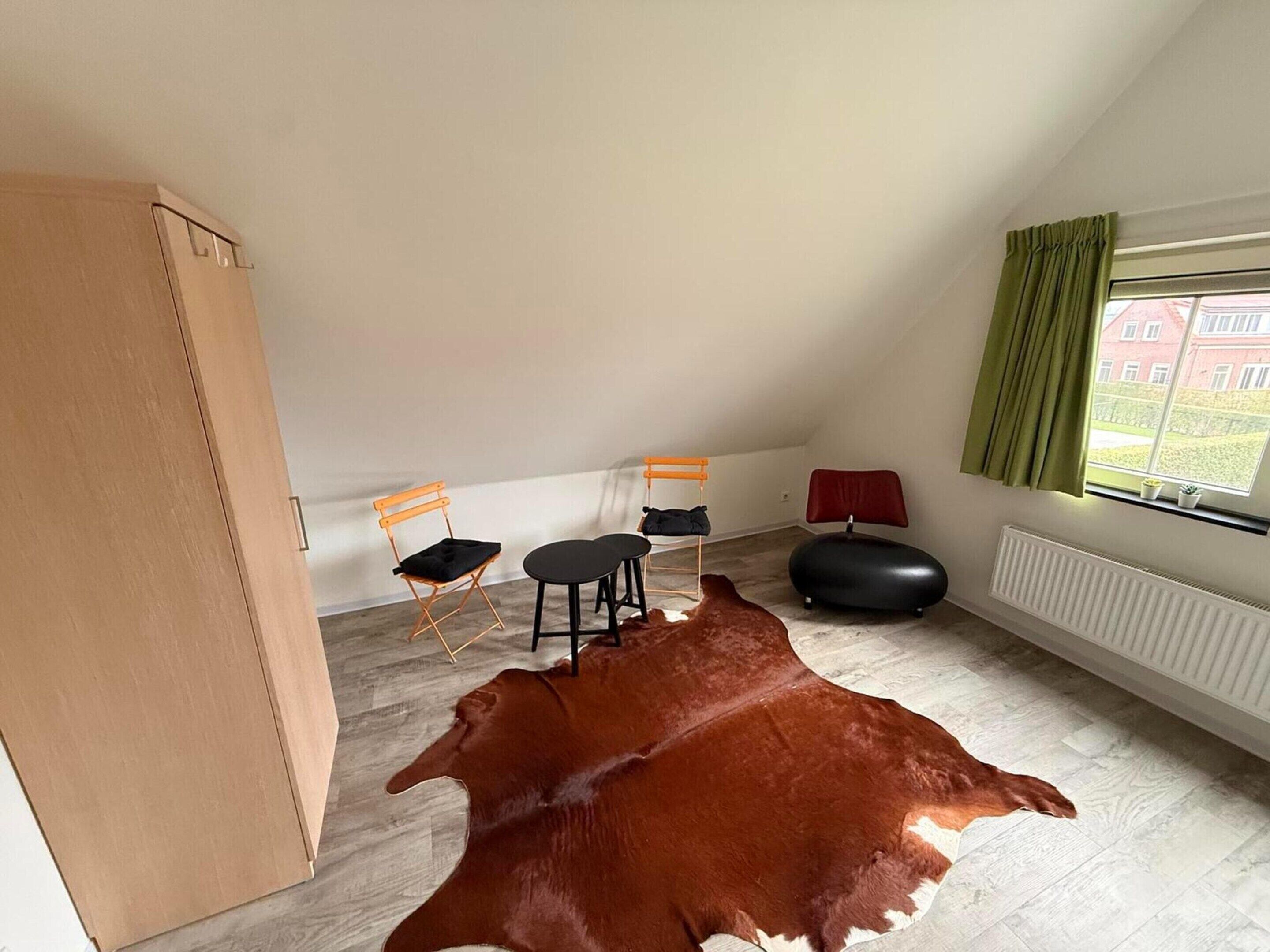 Una habitación con techo inclinado, un gran tapete de cuero marrón, una ventana con cortinas y un radiador.