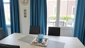 A dining area with a table, chairs, a clock, curtains, and a window view. - Holiday Home in Breskens Near the Beach (Breskens)