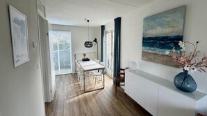 Une cuisine moderne avec un coin repas, un plancher en bois, des meubles blancs et un grand tableau représentant l’océan.