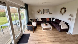 Un salon spacieux avec une porte-fenêtre coulissante donnant sur une terrasse, un canapé de couleur foncée, une table basse blanche et un lampadaire.