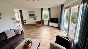 Una sala de estar moderna con sofá, mesa de centro, televisión y un comedor con mesa y sillas.