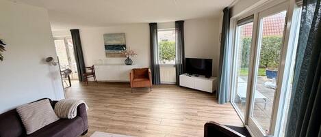 A modern living room with a sofa, coffee table, TV, and a dining area with a table and chairs.