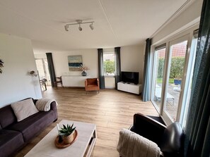 A modern living room with a sofa, coffee table, TV, and a dining area with a table and chairs. - Bungalow in Breskens Near Beach and Dunes (Breskens)